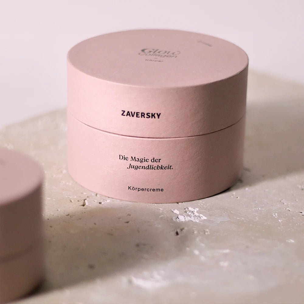 Runde rosafarbene Verpackung der Zaversky Glow Collagen Körpercreme mit Aufschrift „Die Magie der Jugendlichkeit“ auf Steinoberfläche.